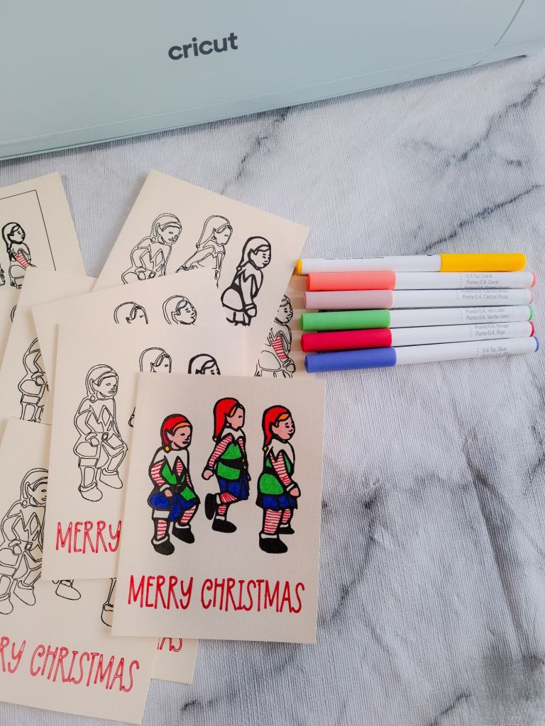 batch of homemade Christmas cards with an elf design, plus Cricut pens and a Cricut Explore machine