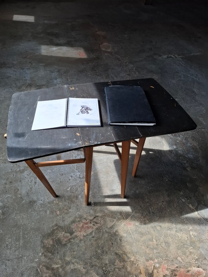 A crooked table in sunlight with notes and a sketchbook on it